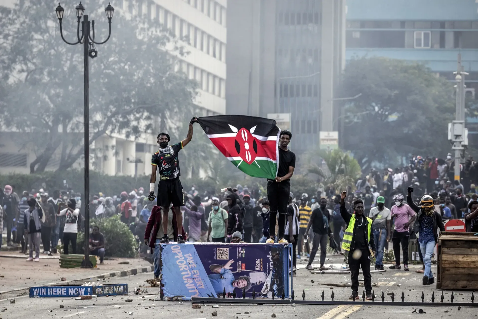 Kenyan Gen Z youth holding Kenya flag on top of sign during protests demanding better country