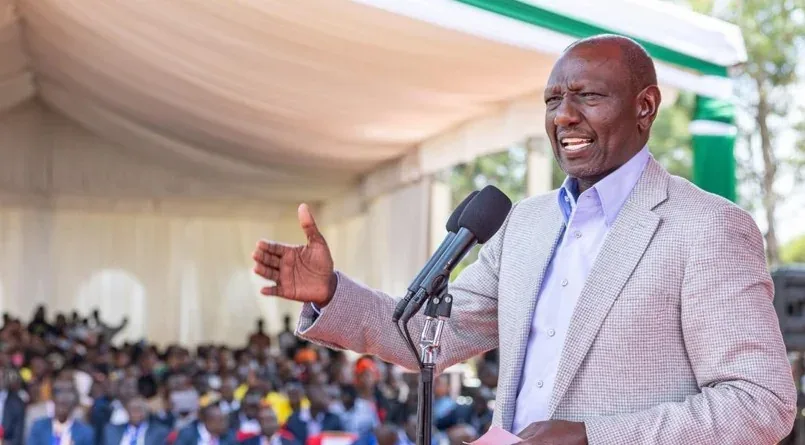 President William Ruto gesturing while addressing a large crowd at a public rally under a tent